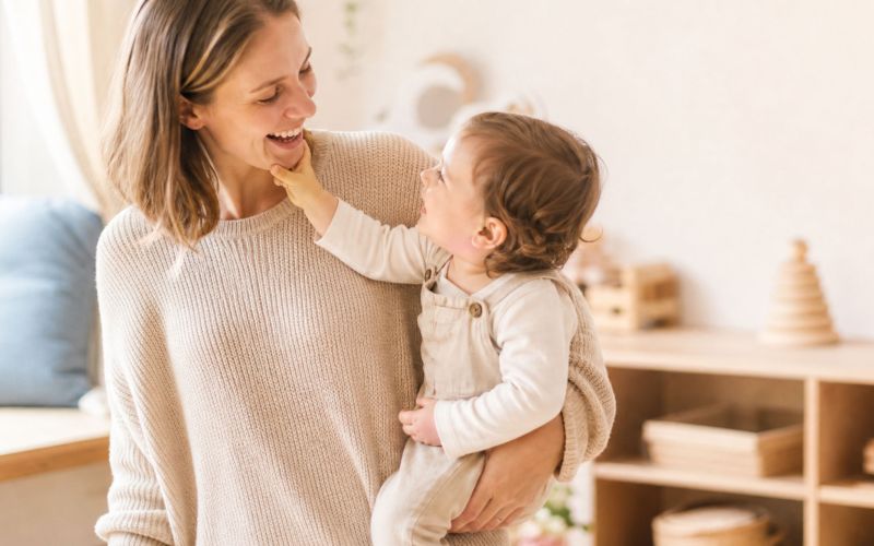 Kinderpflegerin hält ein Kleinkind im Arm, während beide miteinander lachen.