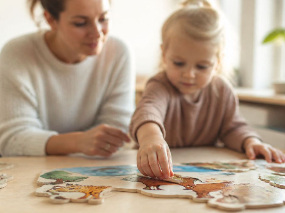 Betreuerin begleitet ein Kleinkind beim Zusammensetzen eines Tierpuzzles.