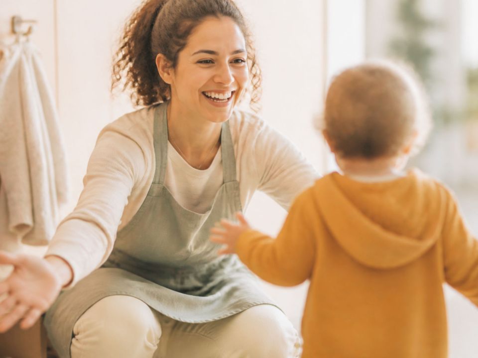 Kinderpflegerin begrüßt ein ankommendes Kleinkind mit offenen Armen.